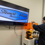 A person creating using 3D Systems' Figure 4 Standalone printer with Stewart-Haas Racing sign in the background.